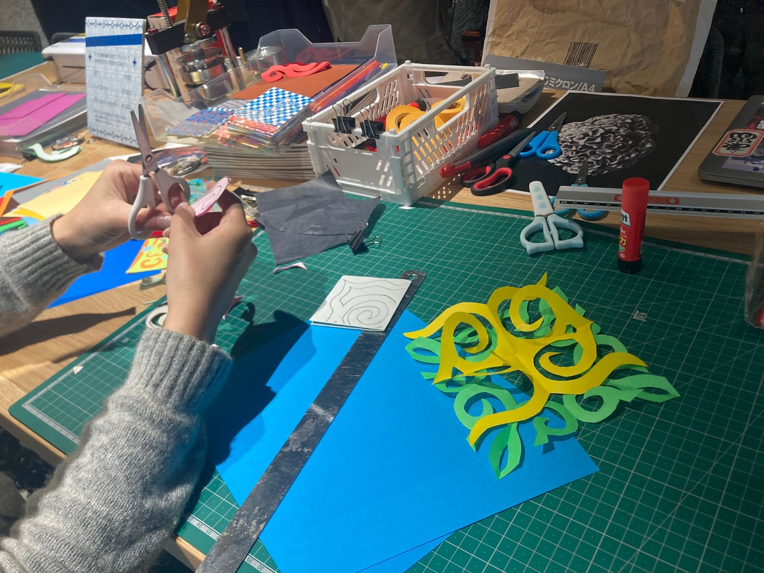Hands cutting a paper pattern on a cutting mat during a collage workshop